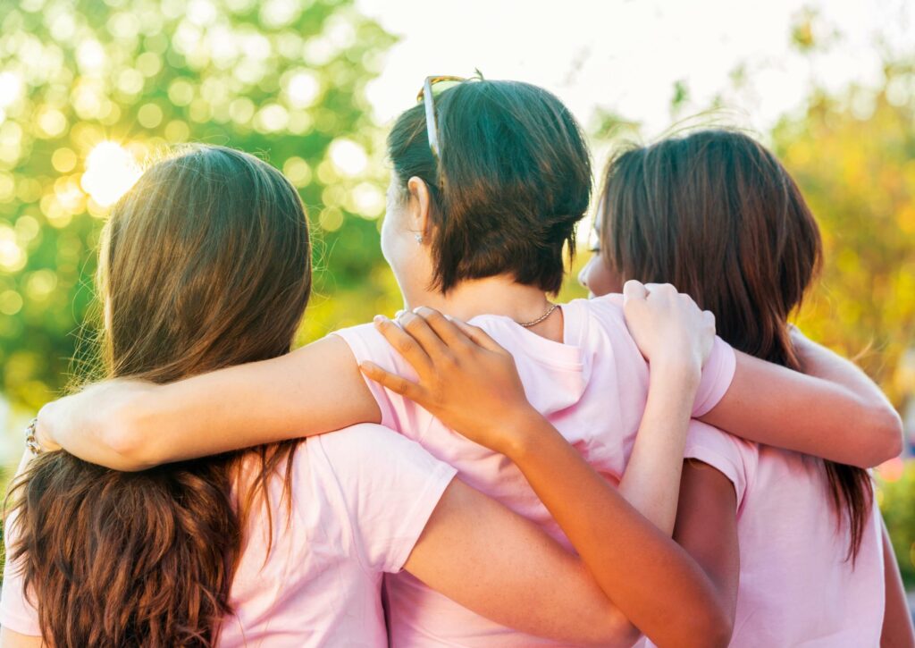 Image taken from behind of three women with their arms around one another.